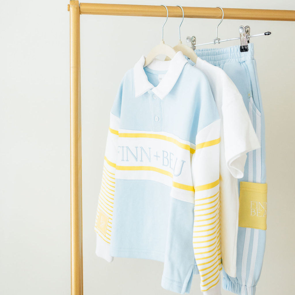 Light blue and yellow striped shirt with 'DINNERS' text on a wooden rack against a white wall.