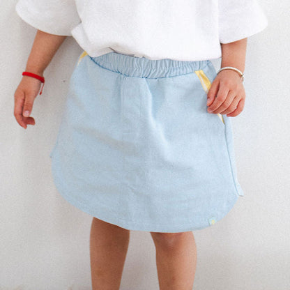 Child wearing a white shirt and light blue skirt against a plain background