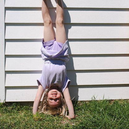 Child hanging upside down against a white wall with grass below