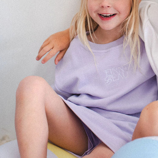 Child wearing a light purple dress sitting on a colorful ball with a plain background