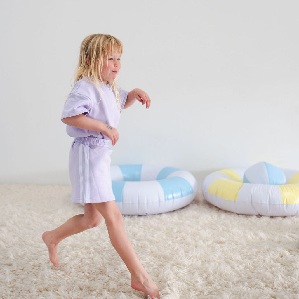 Child in a white robe standing on a carpeted floor with colorful inflatable rings.