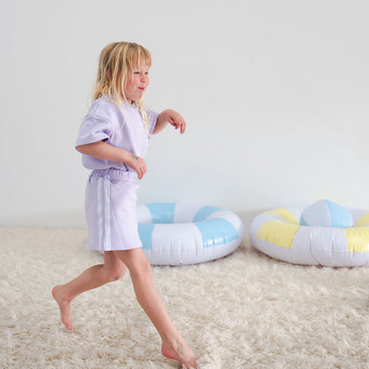 Child in a white robe standing on a carpeted floor with colorful inflatable rings.