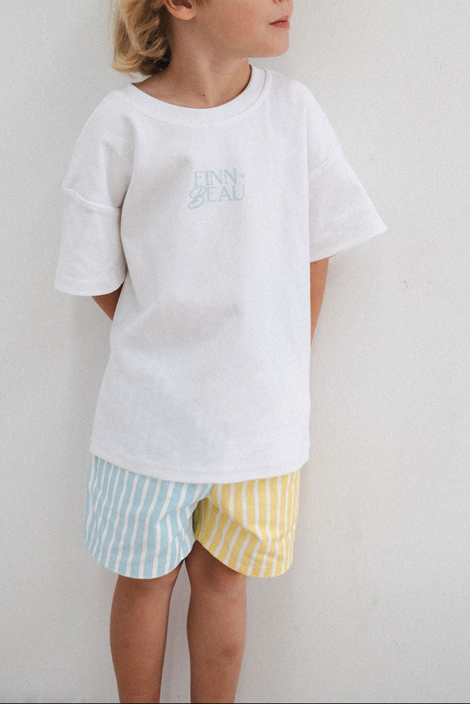 Child wearing a white t-shirt with text and colorful shorts on a plain background