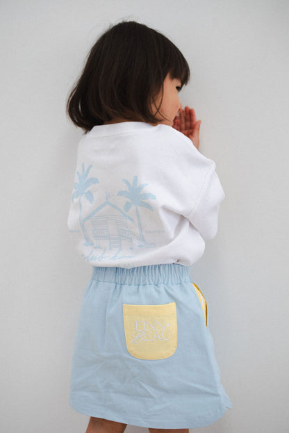 Child wearing a white shirt and light blue skirt against a plain background